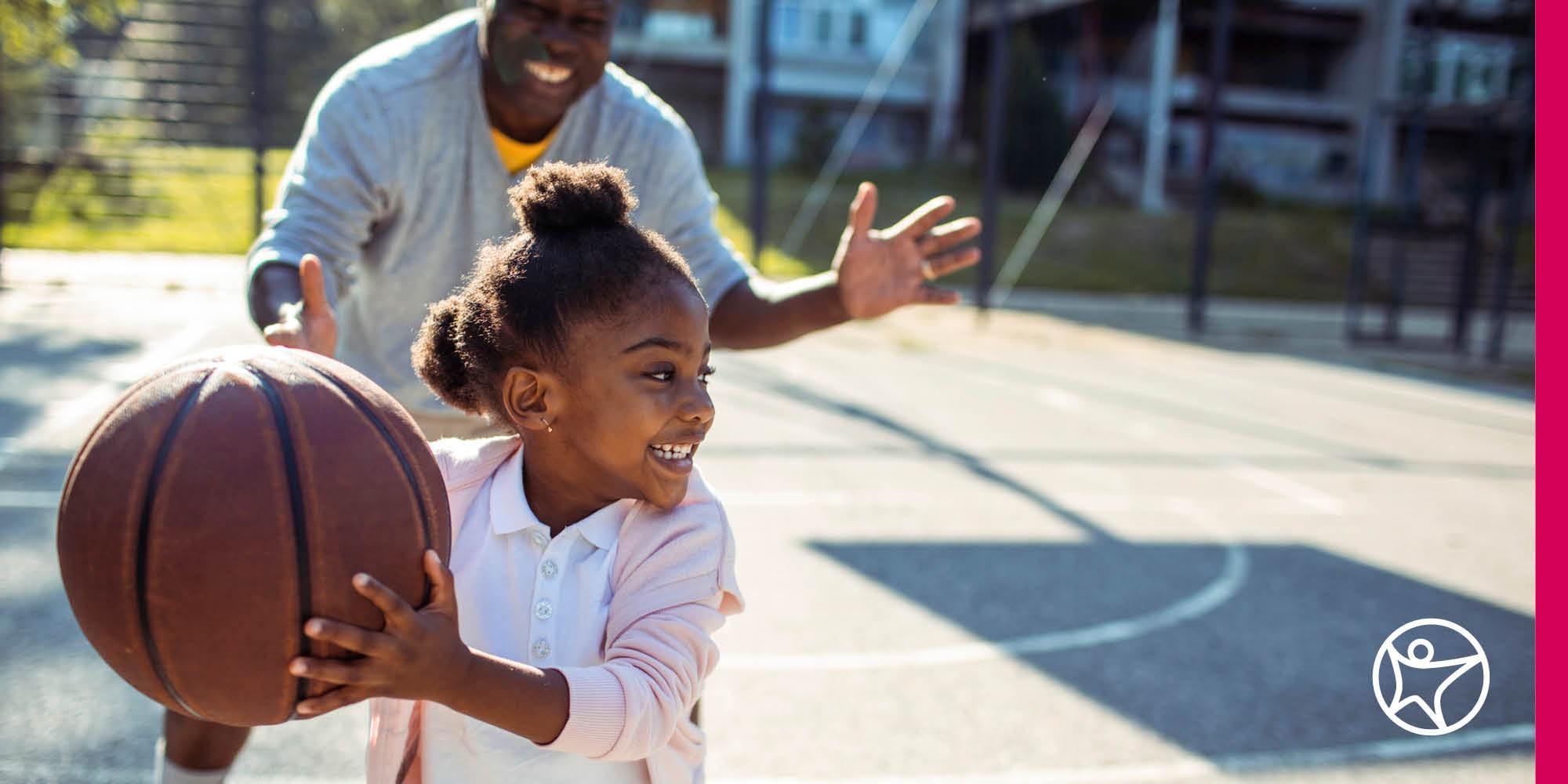 A young girl is playing basketball with her dad